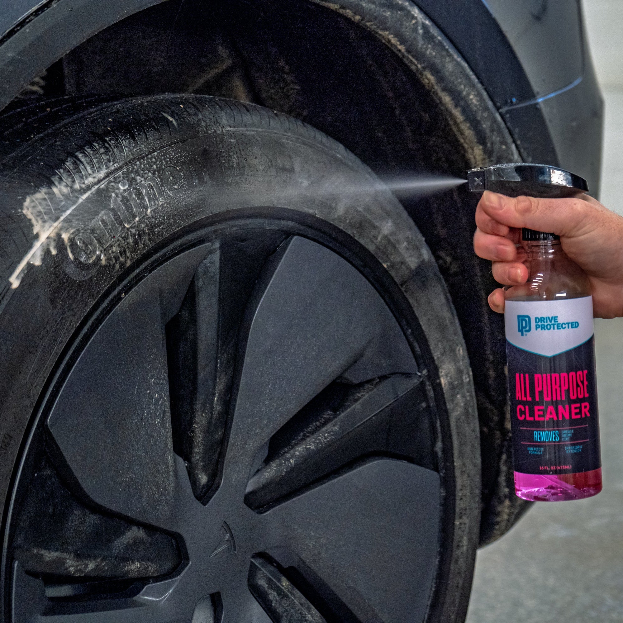 Person cleaning a car tire with a spray bottle labeled 'All Purpose Cleaner'.