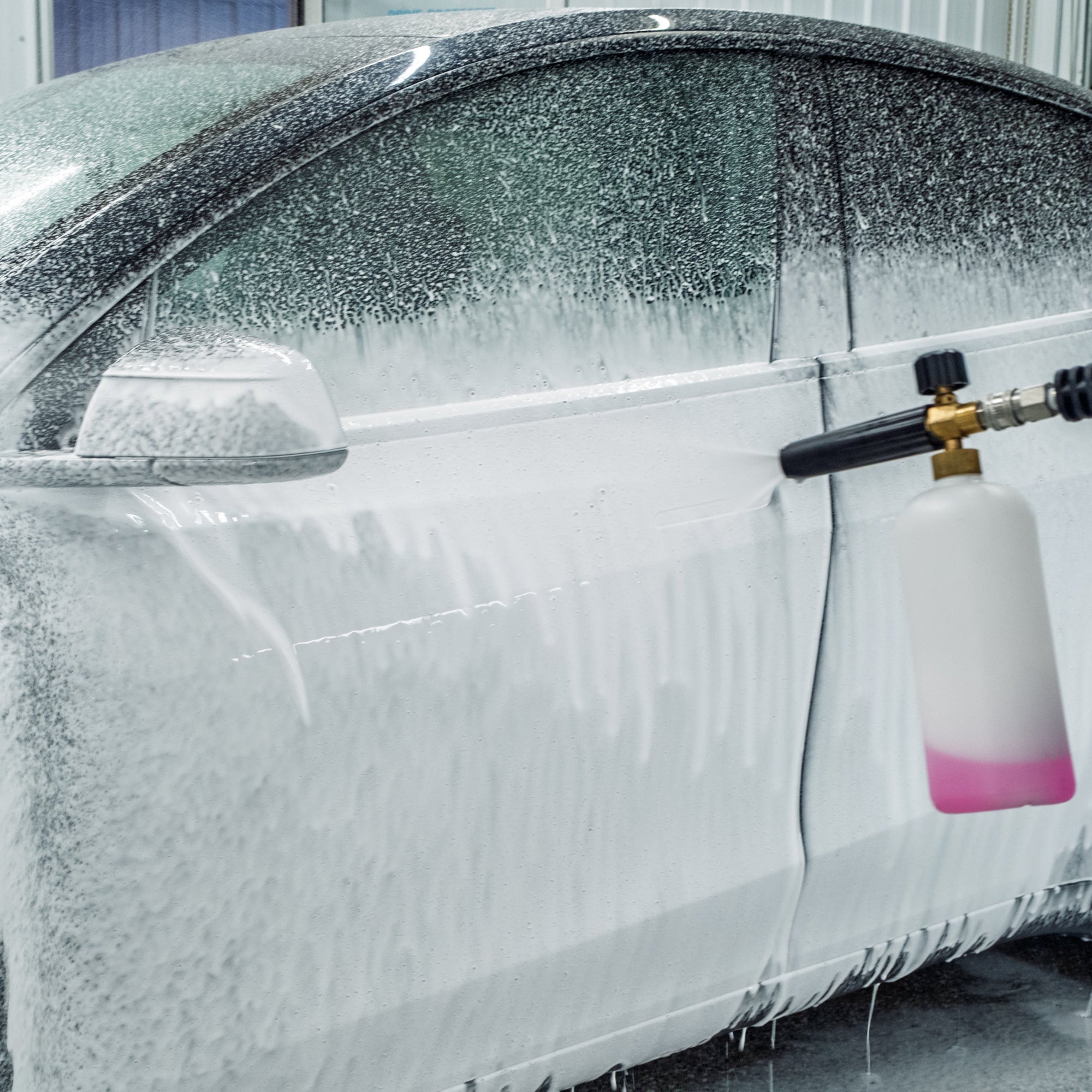 Car being washed with a high-pressure water gun in a garage.