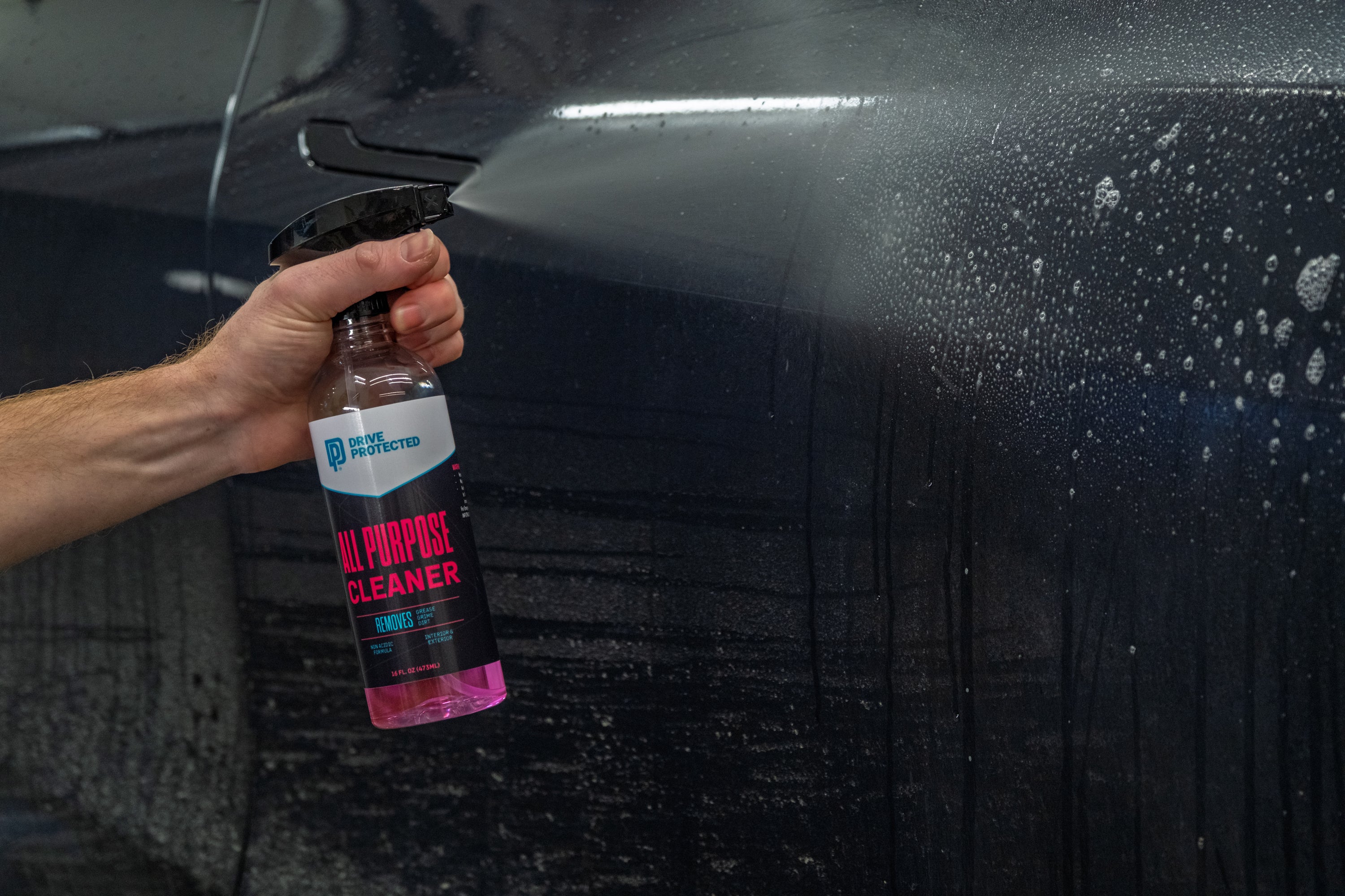 Person holding a bottle of All Purpose Cleaner on a car surface