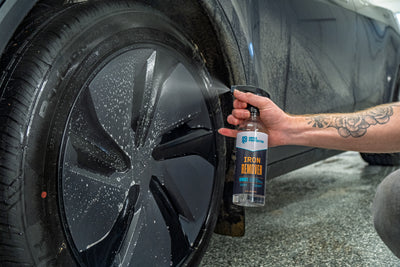Person using a bottle labeled 'Iron Remover' on a car wheel