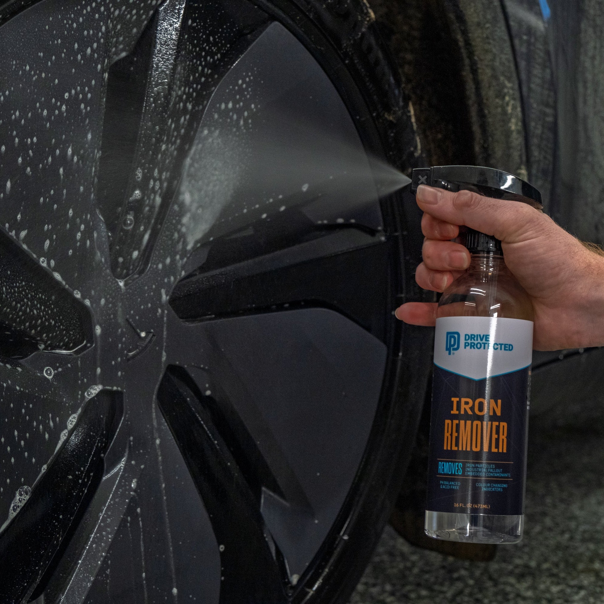 Person holding a bottle of Iron Remover next to a car wheel with water droplets.