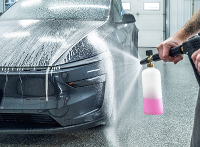 Person washing a car with a pressure washer, focusing on the cleaning process.