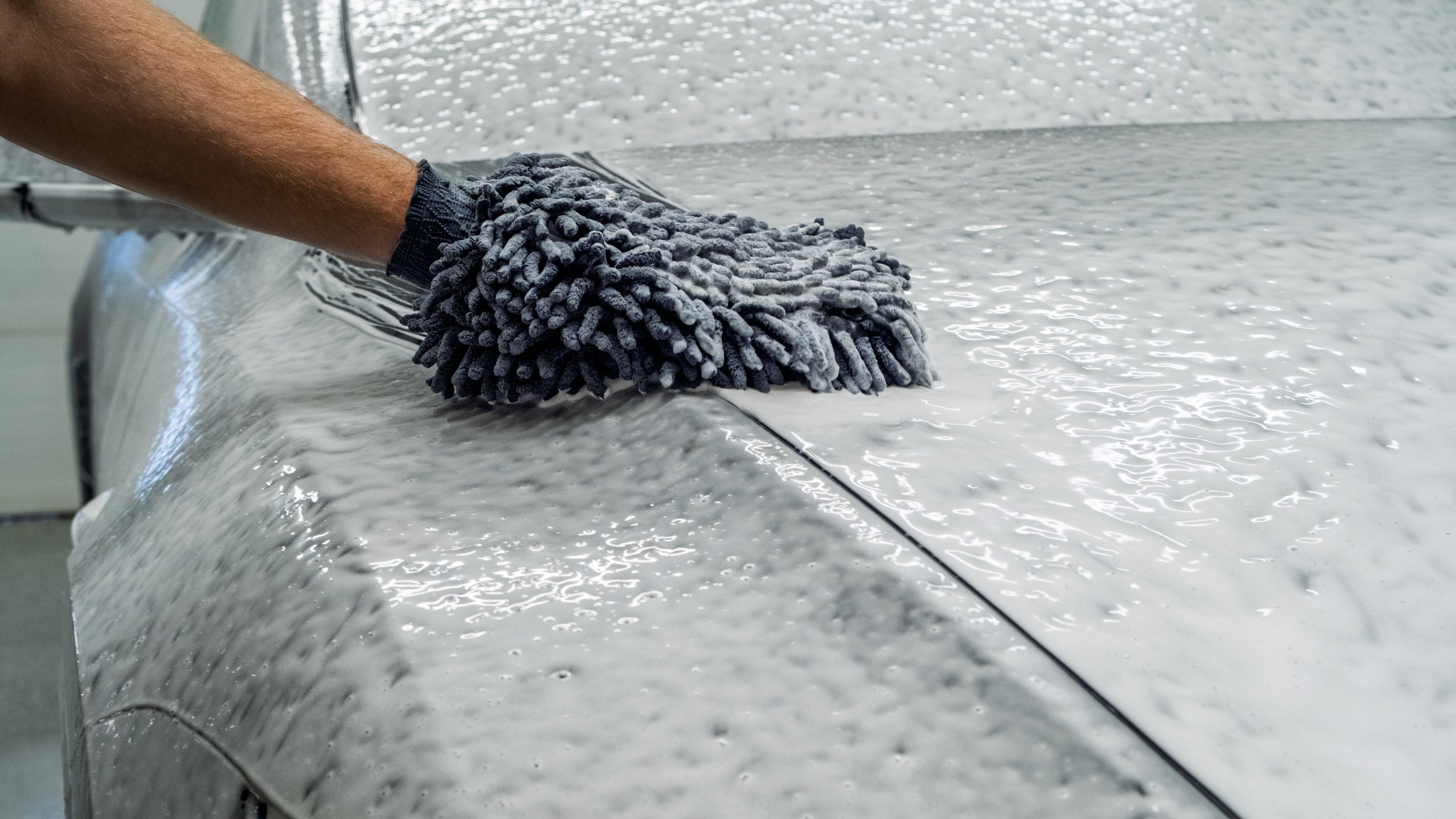 Person cleaning a car with a microfiber towel on a shiny surface