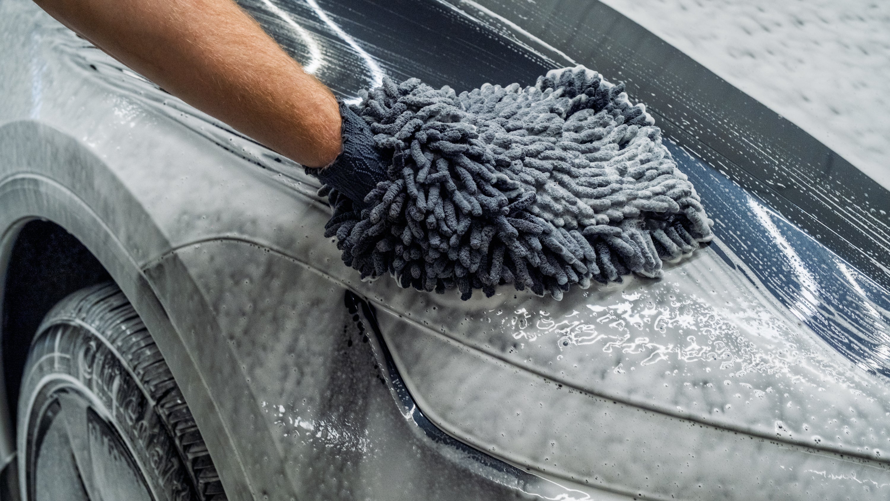 Person cleaning a car with a gray microfiber towel