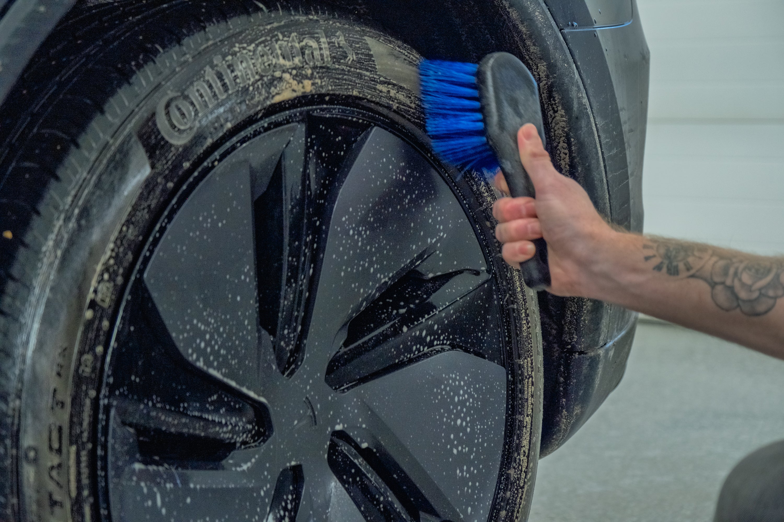 Person cleaning a car tire with a brush