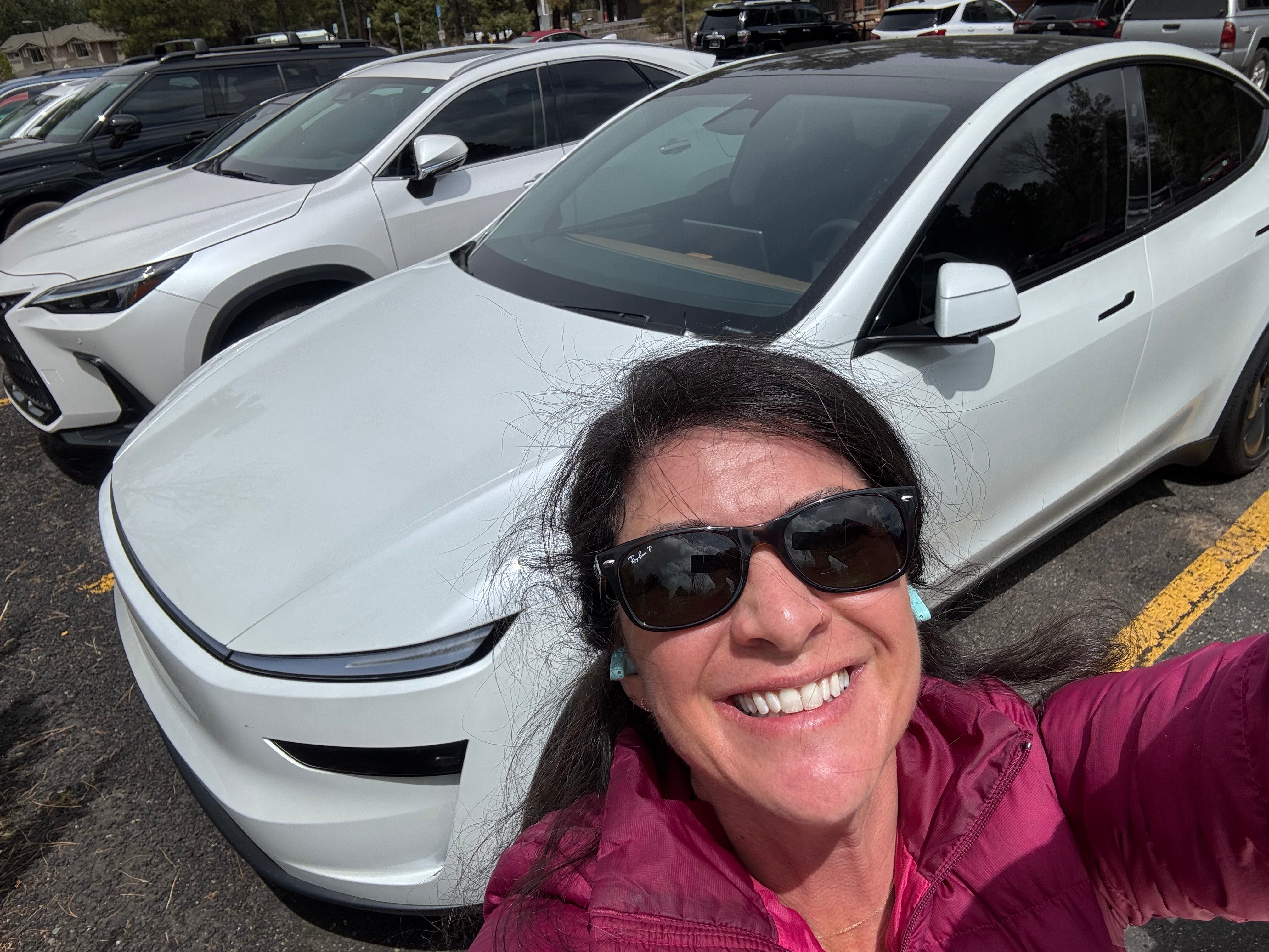 Person taking a selfie in front of a white electric car in a parking lot