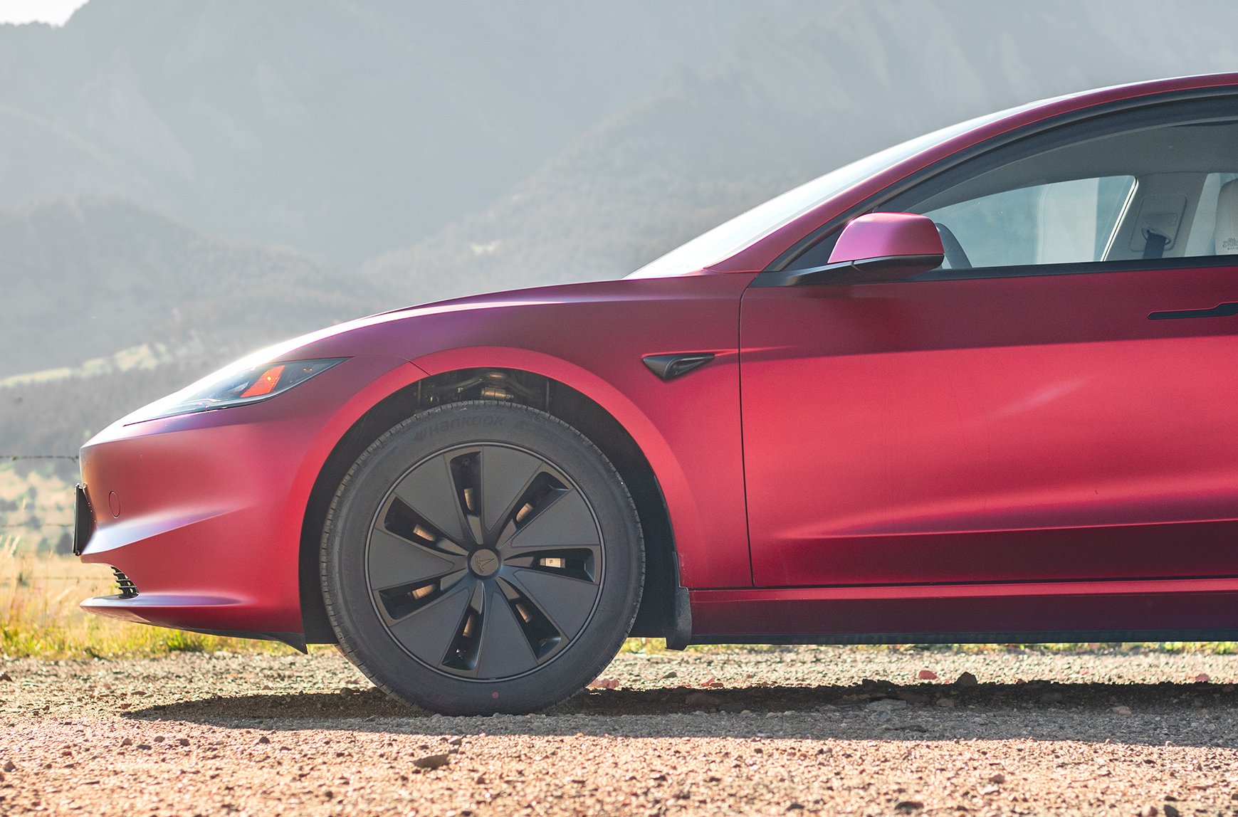 Red Tesla car on a dirt road with mountains in the background