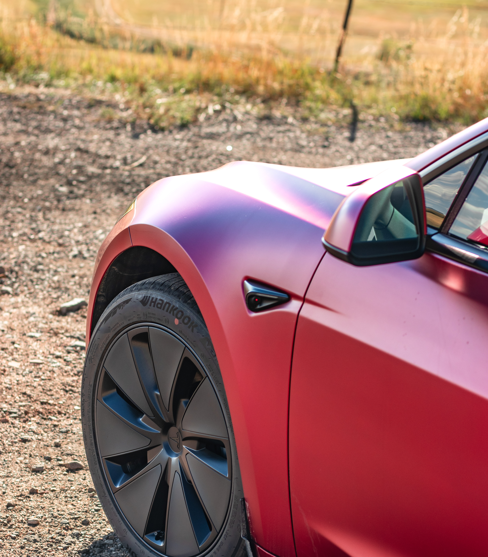 Close-up of a red Tesla Model 3 on a gravel road with a blurred natural background
